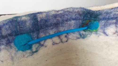 Prachtige witte cocon gemaakt van wol van het melkschaap en merino. De blauwe en paarse details zijn van merinowol.